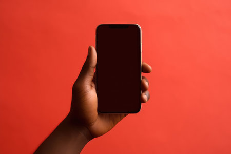 Closeup of African Hand Holding Smartphone on Red Backdropの素材