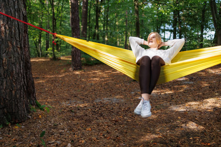 Joyful Girl Relaxing in a Yellow Hammock Amidst Lush Greeneryの写真素材