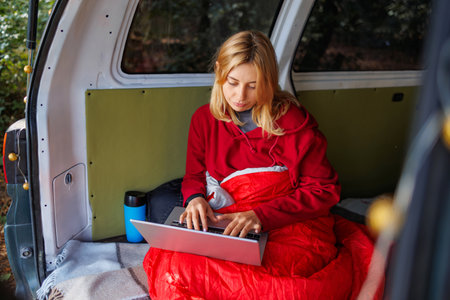 Red-haired young girl working on a laptop in her van in the forest. Remote work conceptの写真素材