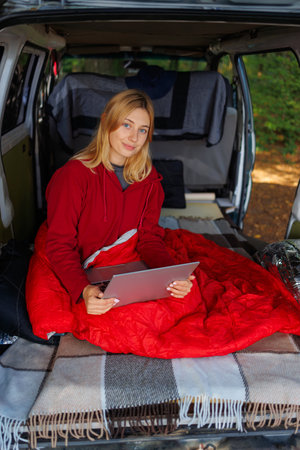 Portrait of a young woman sitting with a laptop in her van at forestの写真素材