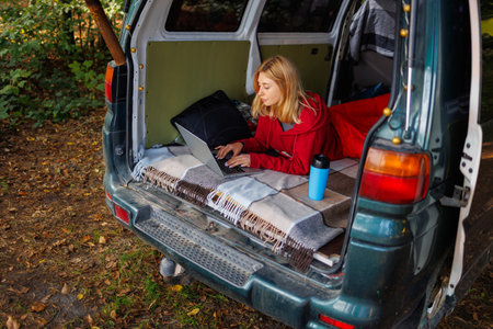 Young woman lying in van with laptop in forestの写真素材