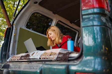 Girl working on a laptop straight from the van while relaxing in nature