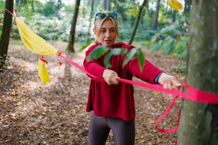 A young woman pulls the ropes of a hammock to a tree while hiking in the forest