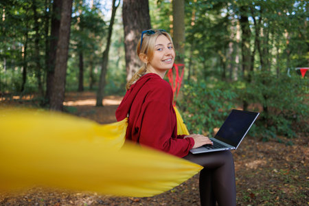 Pretty young female tourist with laptop sitting on hammock in the forest and looking at cameraの写真素材
