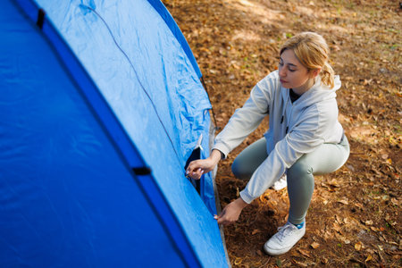 Young woman opening a camping tent in a forest settingの写真素材