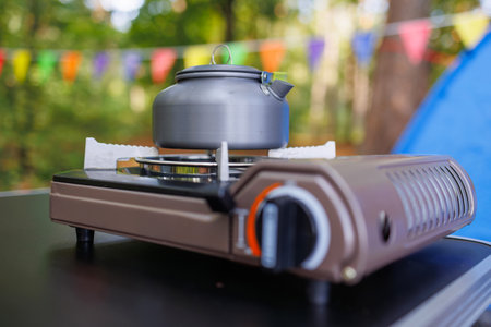 Camping kettle standing on a gas tourist stove against the background of a tent and carnival garlands in the forestの写真素材