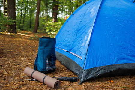 Backpack, trekking poles and sleeping bag lying on the ground near a tent in the forestの写真素材