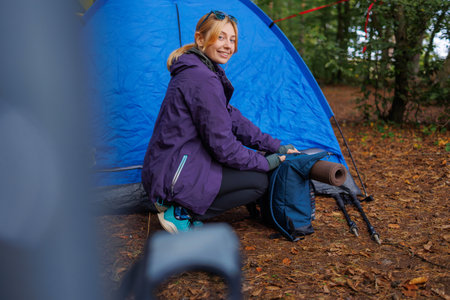 Female tourist in a forest camping is packing a backpack in preparation for a hikeの写真素材
