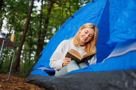 Cheerful girl reading a book in a camping tentの写真素材