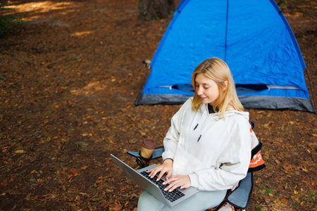 A woman sitting on a chair and working on a laptop during camping in the forestの写真素材