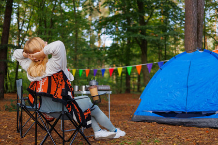Woman in forest camping relaxes while sitting in chair, leaning back and enjoying forestの写真素材