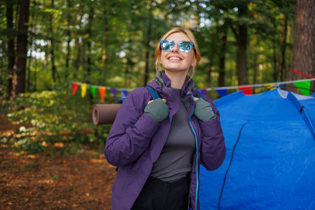 Portrait of a young woman hiker with glasses and a backpack in a forest camping with a tentの写真素材