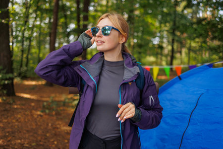 Portrait of a young beautiful tourist woman in glasses with a backpack near a tent in a forest campingの写真素材