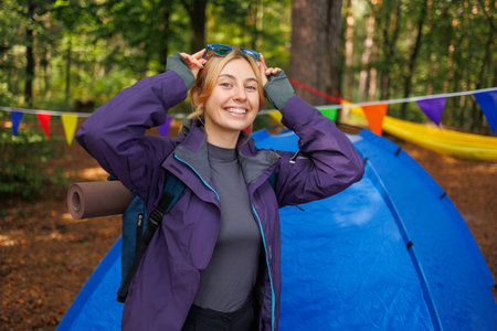 Portrait of a cheerful female tourist posing with a backpack in the forest near a tentの写真素材