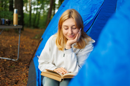 Beautiful young woman in a tent reading a book during a camping stopの写真素材