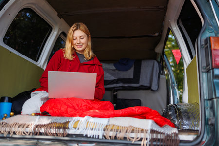 Happy young woman working remotely on a laptop in a van in the middle of the forestの写真素材