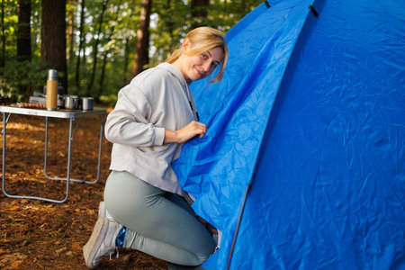 Cute young woman kneeling near a camping tent in the forest looking at the cameraの写真素材