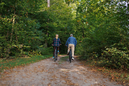 Man and woman are riding a bicycle along a forest roadの写真素材