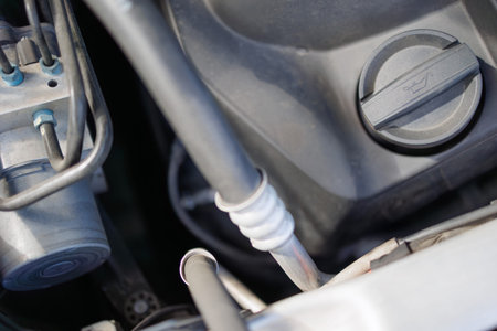 Close-up of car engine oil cap and metal hoses under vehicle hood