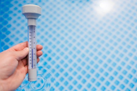 Person holding pool thermometer measuring water temperatureの写真素材