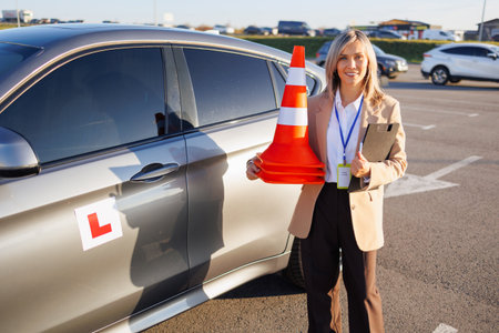 Driving Instructor Holding Cones Beside Training Car in Parking Lotの写真素材