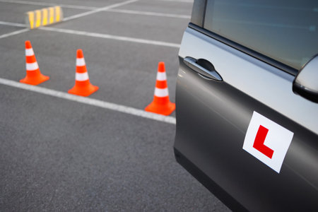 Learner driver vehicle approaching traffic cones during driving school training on an open asphalt areaの写真素材