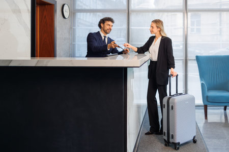 Female guest with suitcase checking into modern hotel at reception counter
