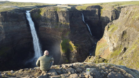 Man sitting in front of a waterfall in Iceland, looking at itの写真素材