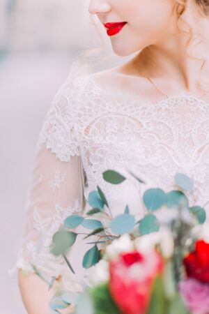 Beautiful bride with bright red lips holds wedding bouquet close up.の写真素材