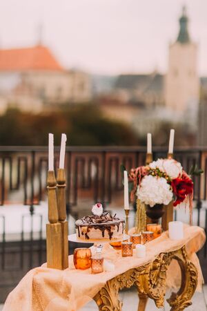 Romantic wedding table with chocolate cake, candles and red flowers. Terrace with view on ancient Lviv architecture.の写真素材