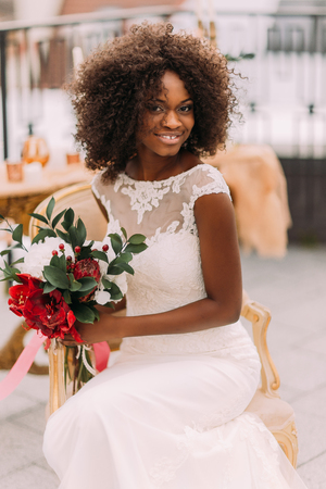 Charming african bride with wedding bouquet in hands cheerfully smiling to the camera.の写真素材