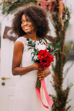 Beautiful african moony bride smiling with bouquet of red flowers on the wedding ceremony.の写真素材