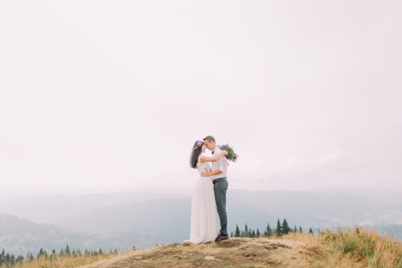 Bride and groom softly hug at the mountain peak. Breathtaking photo.の写真素材