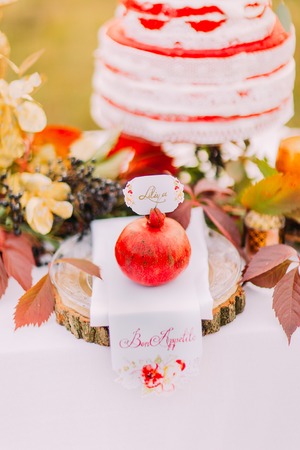 Big red pomegranate on the wedding table close up with wedding cake on background.の写真素材