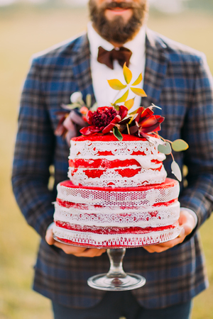 Stylish bearded groom with delicious wedding cake in hands closeup.の写真素材