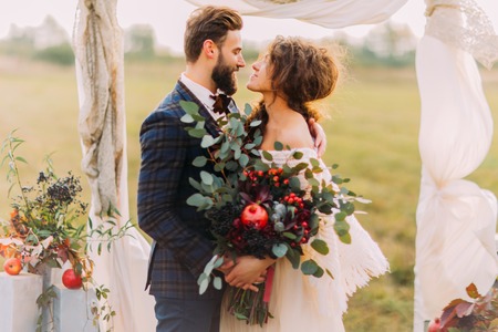 Happy wedding couple lovingly look at each other during  ceremony on the meadow.の写真素材