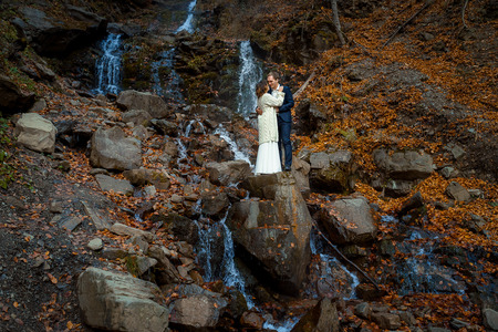 Charming bride and groom stanging on the waterfall. Beautiful autumn forest background.の写真素材
