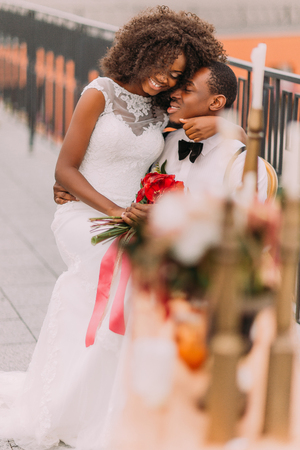 Black cheerful wedding couple softly hugging on the terrace with amazing view on Lviv ancient architecture. Wedding day.の写真素材