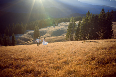 Beautiful wedding couple running and having fun on the field surrounded by mountains.の写真素材