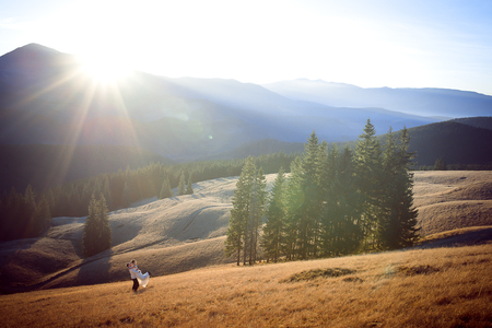 Happy groom holds in hands his beautiful bride. Wonderful mountains landscape.の写真素材