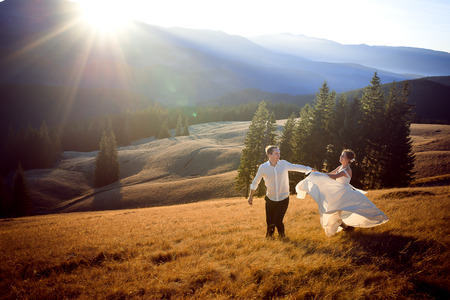 Beautiful wedding couple running and having fun on the field surrounded by mountains.の写真素材