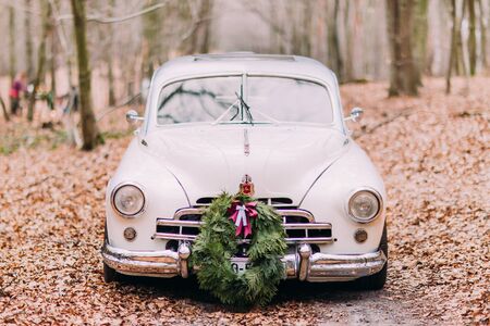 White vintage wedding car decorated with wreath in the autumn forest.の写真素材