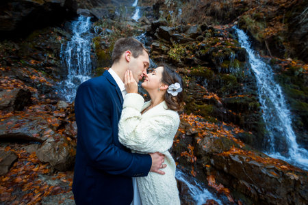 Wedding couple softly hugs on the waterfall. Misty day in mountains.の写真素材