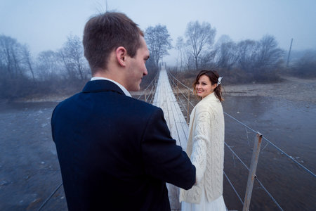 Lovely wedding couple holding hands on the suspension bridge. Honeymoon in mountains.