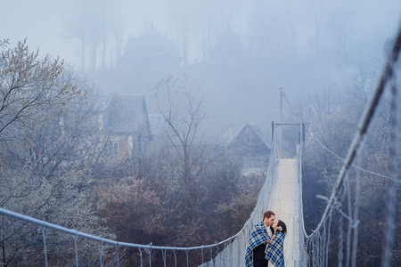 Charming wedding couple wrapped in blanket softly kiss on the sospension bridge at mountains. Autumn mountains background.の写真素材