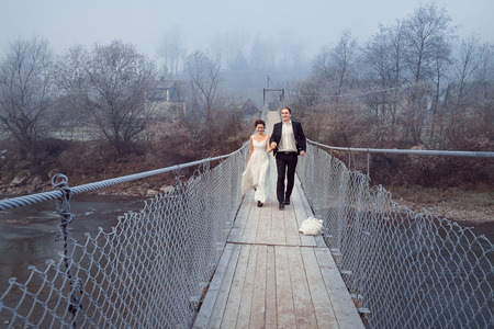 Cheerful newlyweds walking and laughing on the wooden bridge. Honeymoon at mountains.の写真素材