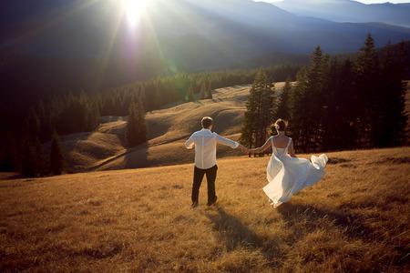 Happy wedding couple running and having fun on the field surrounded by mountains.の写真素材
