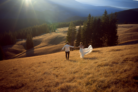 Happy wedding couple running and having fun on the field surrounded by mountains.の写真素材