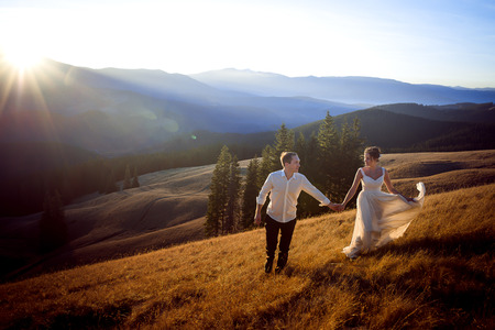Beautiful wedding couple running and having fun on the field surrounded by mountains.の写真素材