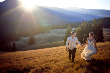 Beautiful wedding couple running and having fun on the field surrounded by mountains.の写真素材